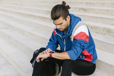 Full length of young man using mobile phone while sitting outdoors