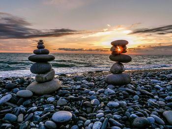 Stones on pebbles at beach against sky during sunset
