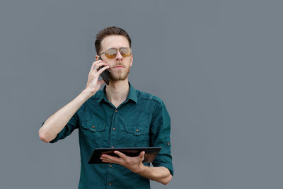 A young man holds a tablet in his hands, reads information on the tablet and talking on the phone