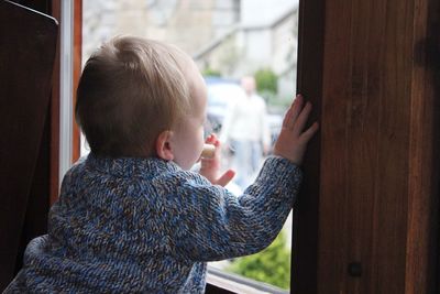 Rear view of baby boy looking through window at home