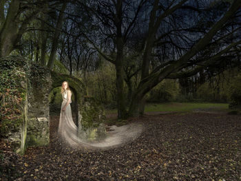 Side view of woman standing by trees in forest