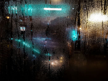 Illuminated lights seen through wet glass window at night