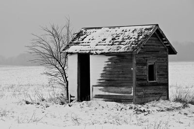Abandoned house on snow covered field against sky