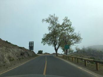 Empty road amidst trees on field against clear sky