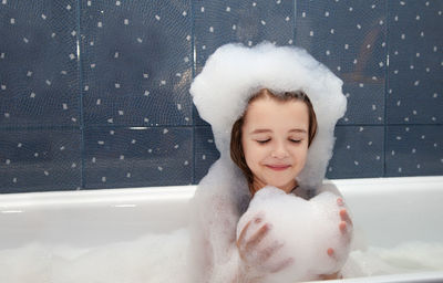 Smiling girl playing with soap sud in bathtub