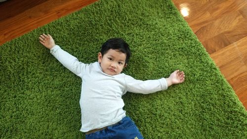 High angle view of smiling boy lying on carpet