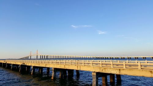 Silhouette pier over river against blue sky