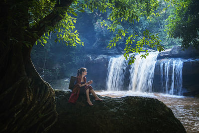 Woman sitting by waterfall in forest