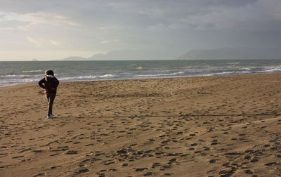 Rear view of man standing on beach against sky