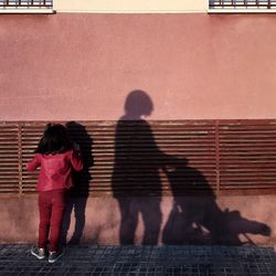 Rear view of girl standing by wall on street