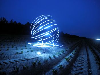 Light trails on landscape against clear blue sky at night