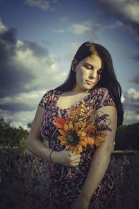 Young woman standing by flowering plants on field against sky