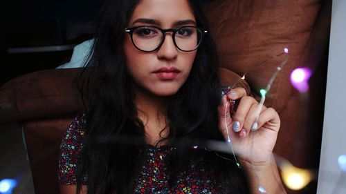 Portrait of young woman wearing eyeglasses while holding string light