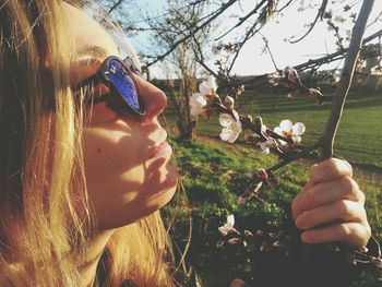 Side view of woman smelling cherry blossoms on twig