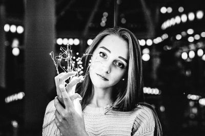 Portrait of beautiful young woman holding illuminated string light