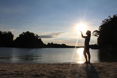 Silhouette of woman standing by lake during sunset