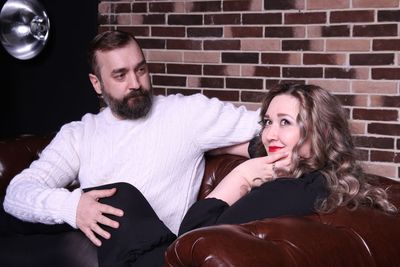 Man looking at thoughtful woman sitting on sofa against brick wall