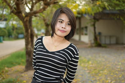 Beautiful young woman looking away while standing against trees in park