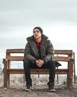 Young man sitting on a bench with his hands clasped