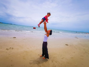 Full length of happy mother and baby on beach against sky