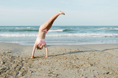 Teenager performing cartwheel at beach against sky