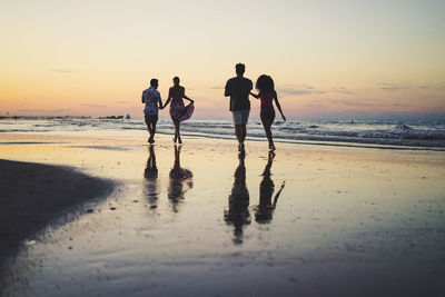 Rear view of couples walking on shore at beach during sunset