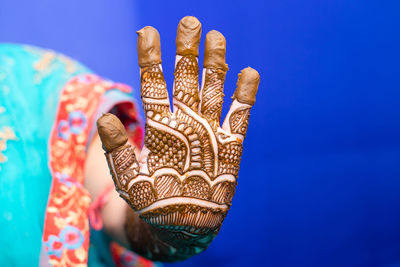 Midsection of bride with henna tattoo against blue background