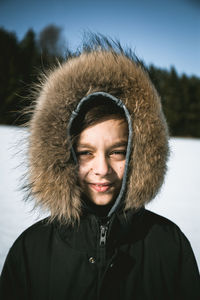 Portrait of smiling boy standing on snow field against sky