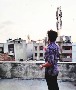 Rear view of man standing by buildings against sky