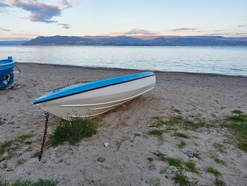 Boat moored on beach against sky during sunset