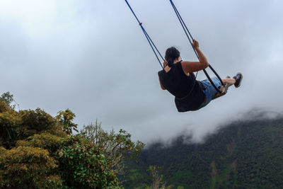 Rear view of woman playing on swing against sky