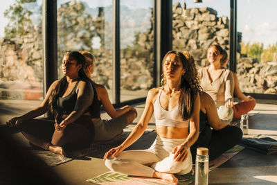 Female friends exercising while sitting back to back at retreat center