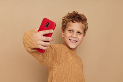 Smiling boy taking selfie with smart phone by brown background