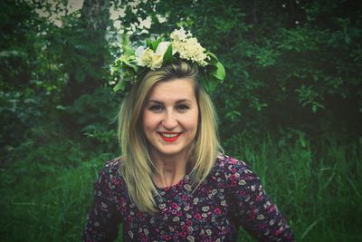 Portrait of happy beautiful woman wearing flowers while standing against plants