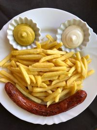 High angle view of french fries with dip and sausages arranged in plate on table