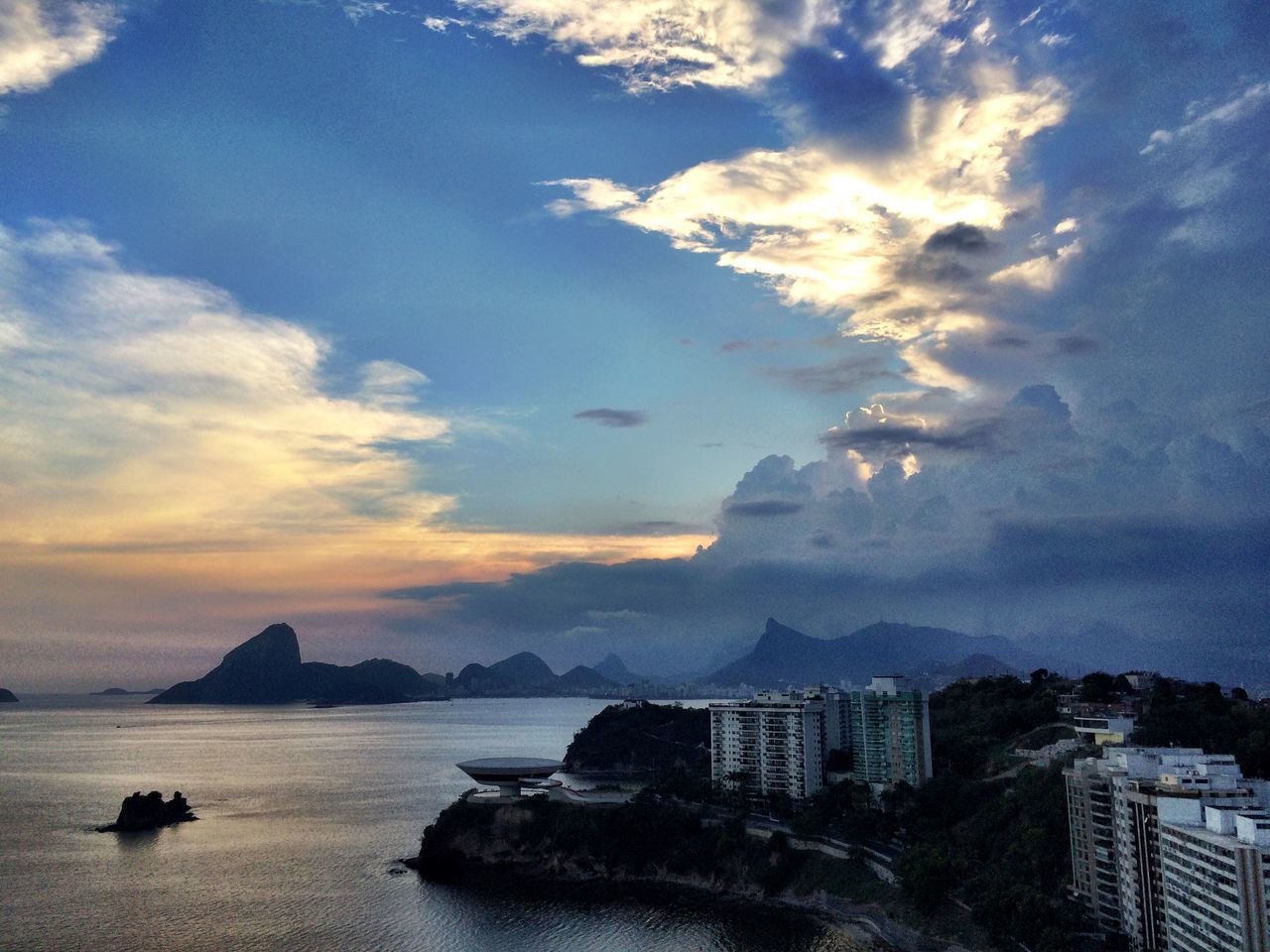 building exterior, sky, mountain, water, cloud - sky, architecture, built structure, scenics, beauty in nature, mountain range, city, sea, cloudy, cloud, nature, cityscape, sunset, tranquil scene, tranquility, waterfront