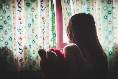 Rear view of woman looking through window at home