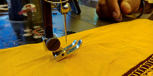 Cropped hand sewing yellow textile on machine