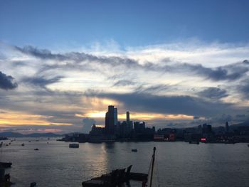 Sea by city buildings against sky during sunset