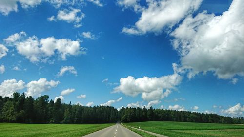 Empty road amidst field against sky