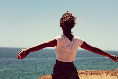 Woman with arms outstretched standing at beach against clear sky