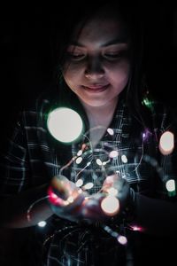 Young woman holding illuminated string lights in dark