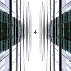 Low angle view of airplane in flight and tall buildings