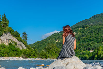Rear view of woman sitting on mountain against sky