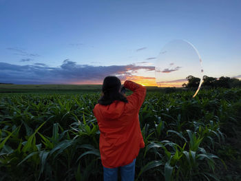 Rear view of woman standing on field against sky during sunset