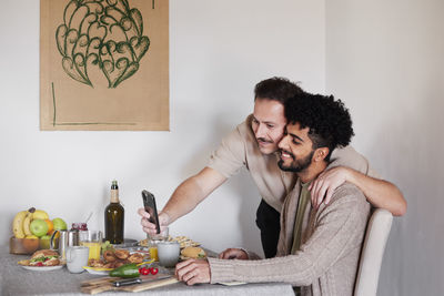 Homosexual couple sitting at table and taking selfie