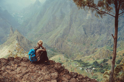 Woman sitting on rock against mountains