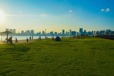 People on grassy field by buildings in city against sky