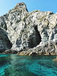 Rock formation in sea against clear blue sky