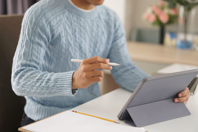 Midsection of woman holding mobile phone while sitting on table